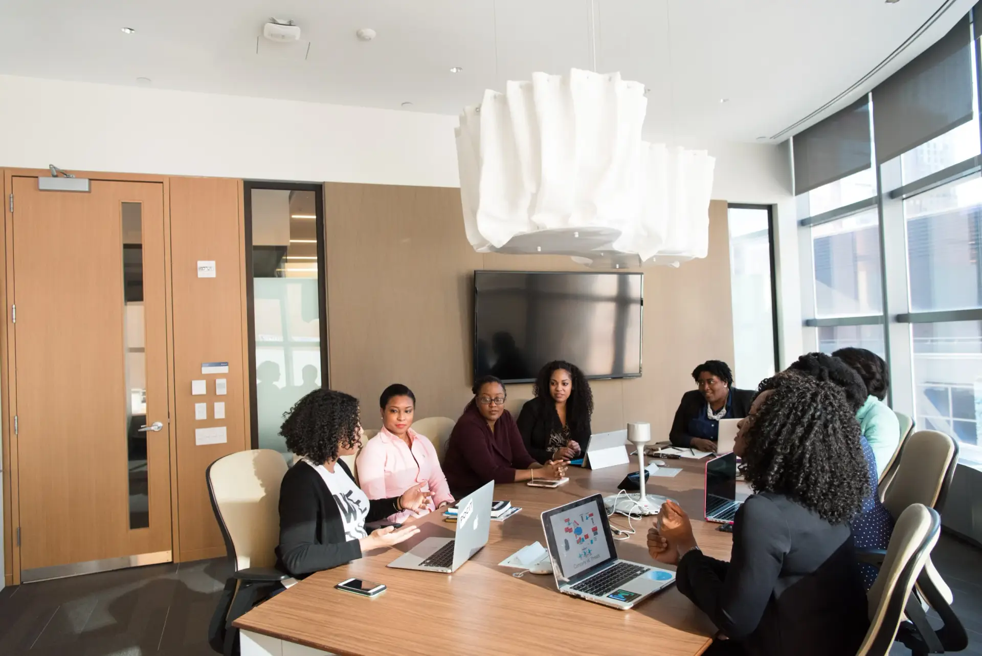 A group of African American women sitting in a conference room with their laptops having a discussion.